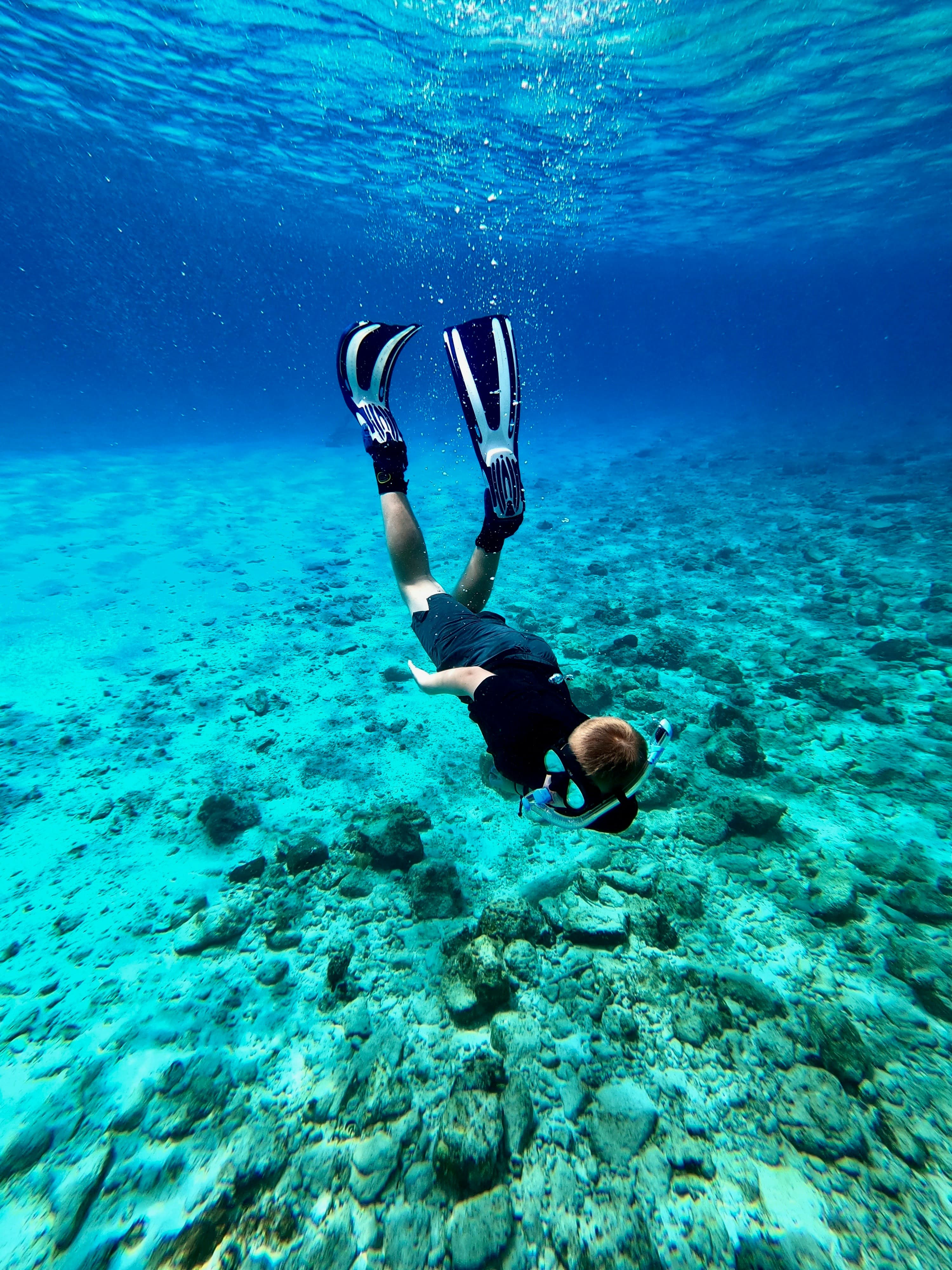 A snorkeler diving down over a shallow reef in vivid turquoise water