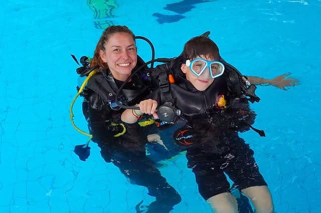An instructor holding a child's hand during a pool scuba introduction